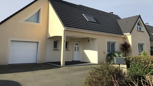 Een tweelaags huis met een garage, een klein portaaltje en een zonnepaneel op het dak.