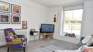 Una sala de estar con un sofá, un sillón colorido, un televisor y cuadros en la pared.