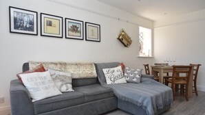 Un sofá gris con varios cojines, una mesa de comedor con sillas y cuadros en la pared.