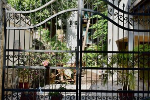 A wrought iron gate with a view of a courtyard featuring potted plants and a wooden deck.