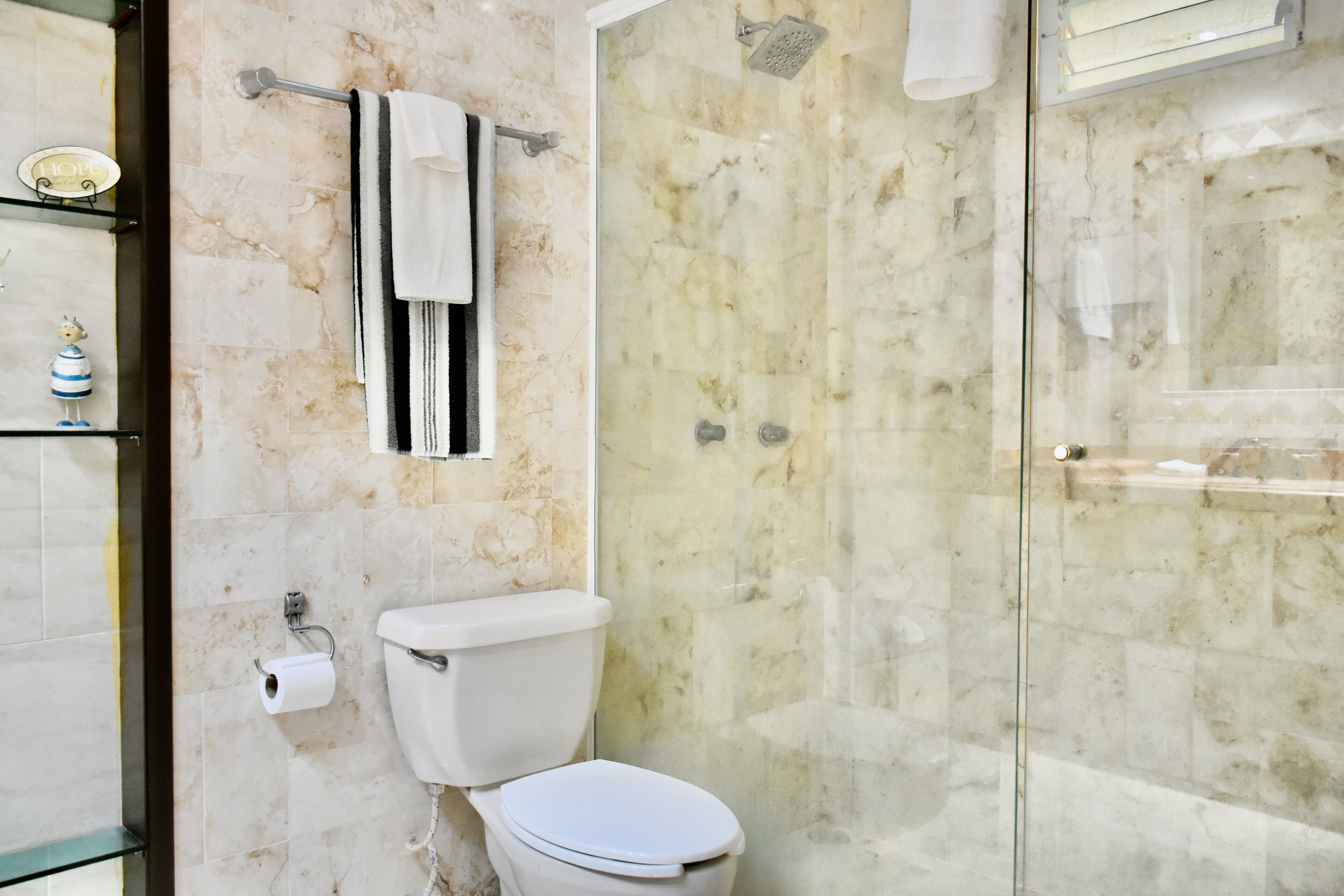 A bathroom with a toilet, a glass shower enclosure, and marble walls.