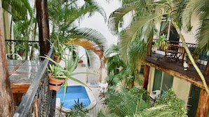 Un exuberante jardín interior con piscina, terraza de madera y plantas en macetas.