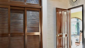 Un dormitorio con cama, contraventanas de madera, una puerta y vistas a un espacio exterior.