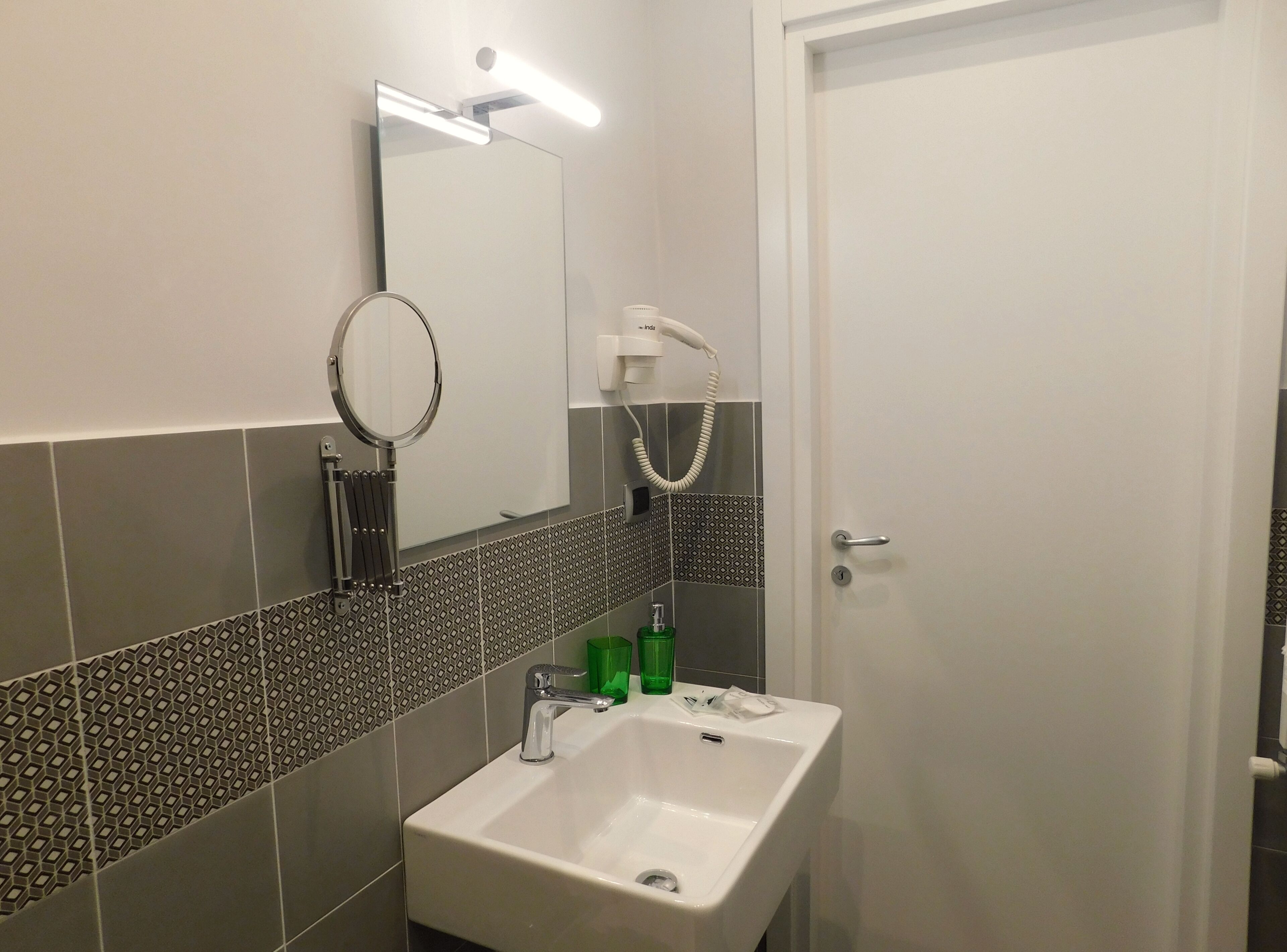 Ein Badezimmer mit weißem Waschbecken, einem Spiegel, einem Handtuchhalter und einer Dusche mit Duschbrause.