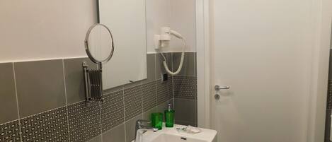 Un baño con lavamanos blanco, espejo, toallero y ducha con cabezal de ducha manual.