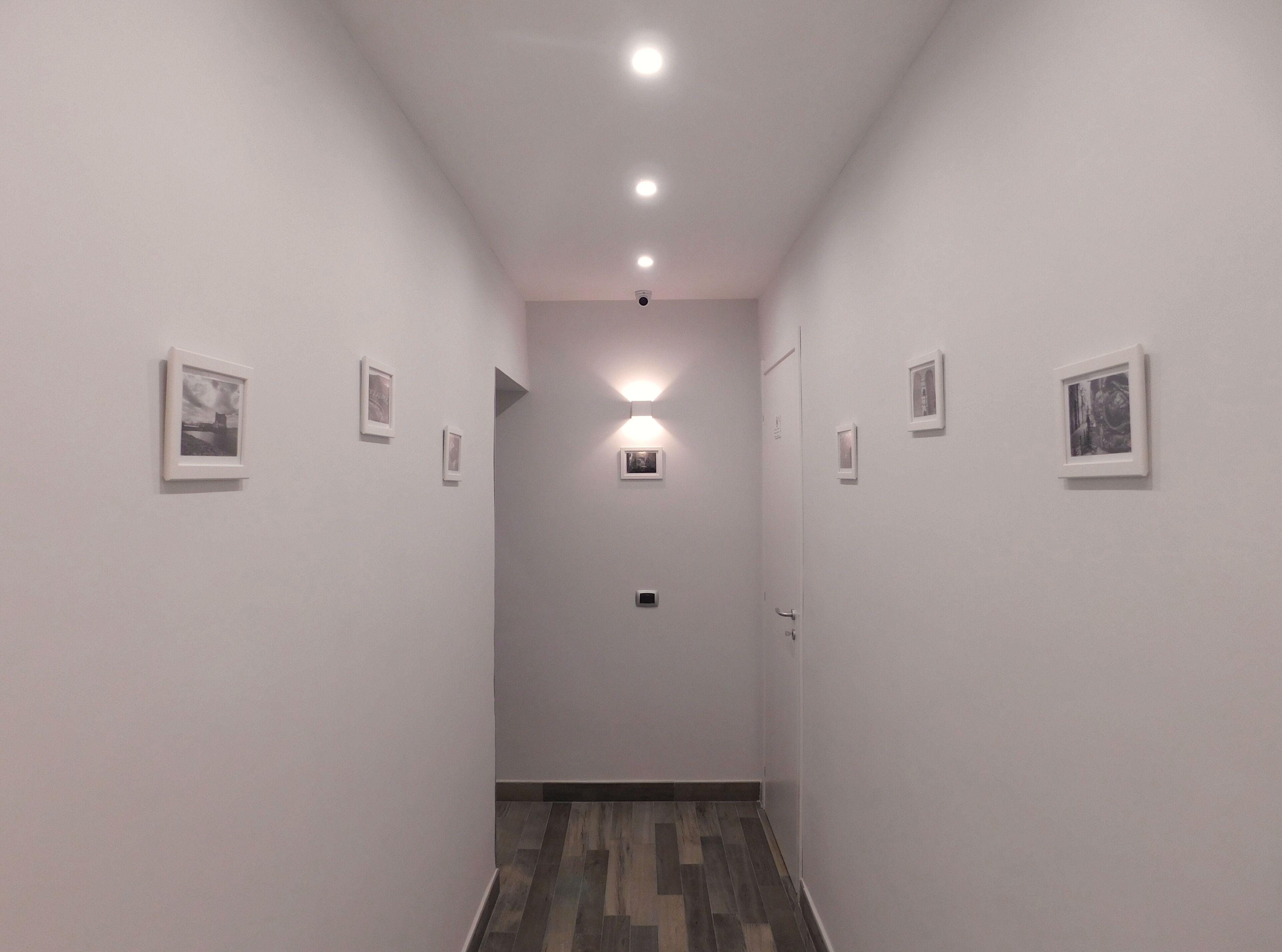 A narrow hallway with white walls, small framed pictures, and a wooden floor.