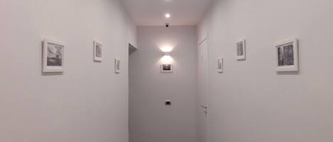A narrow hallway with white walls, small framed pictures, and a wooden floor.