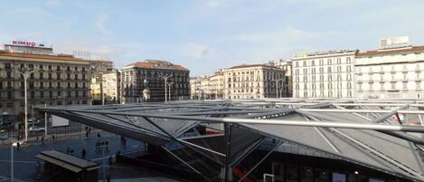 A modern architectural structure with a glass roof, surrounded by urban buildings and a clear sky.