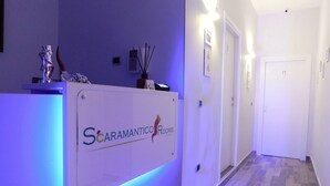 A reception area with a sign for 'Scaramantico Rooms' and a hallway with a wooden floor and white walls.