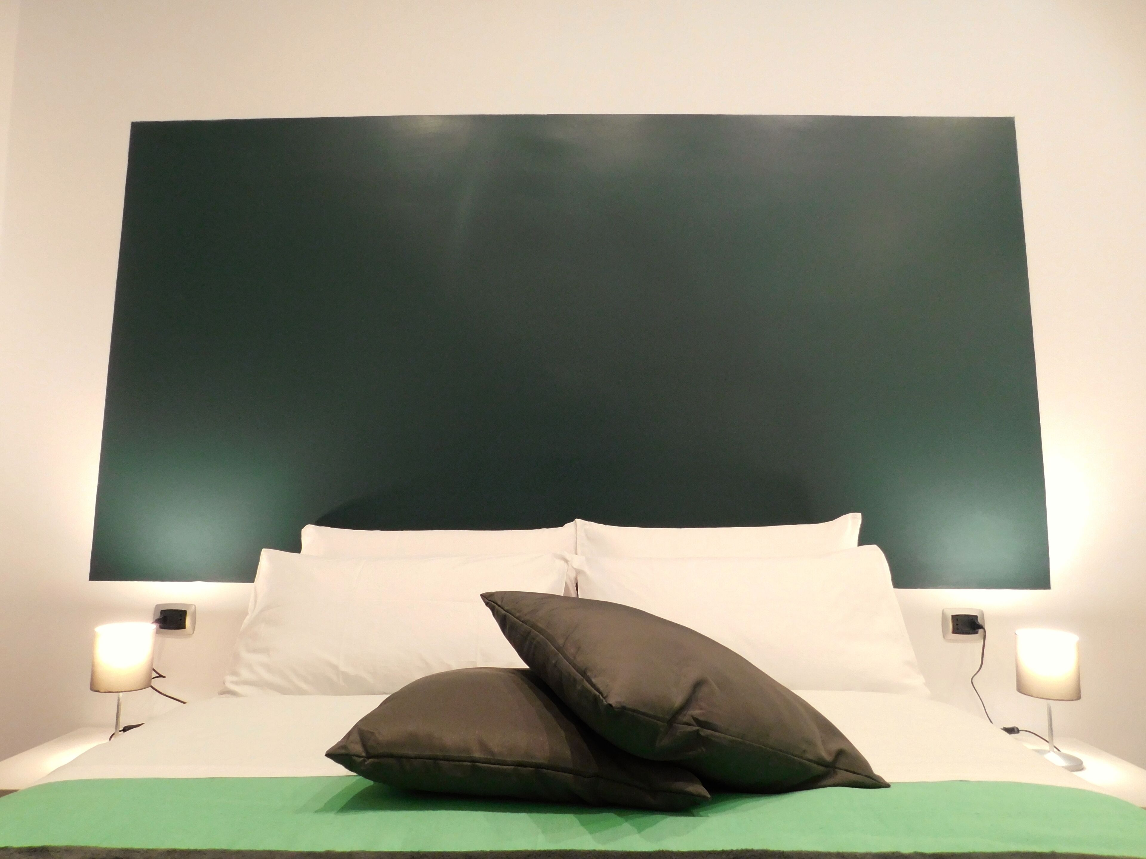 A bed with white bedding, two dark pillows, and two bedside lamps.