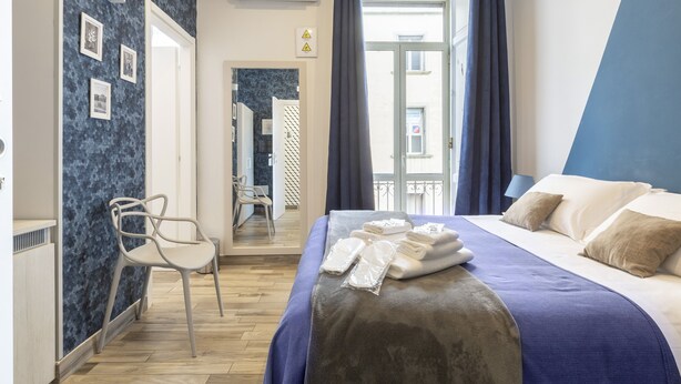 A hotel room with a bed, a chair, a bathroom visible through an open door, and a view of the outside.