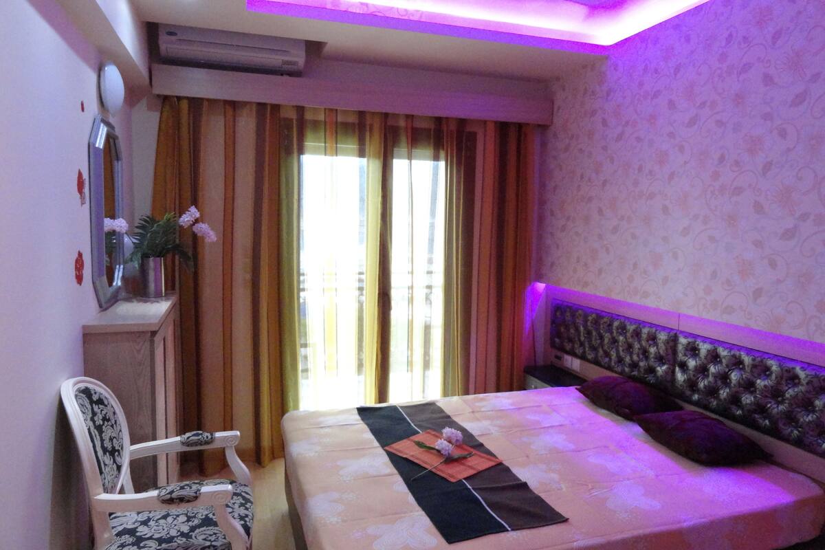 A hotel room with a bed, a chair, a desk with a mirror, and a window with curtains.