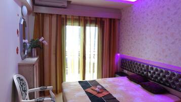 A hotel room with a bed, a chair, a desk with a mirror, and a window with curtains.
