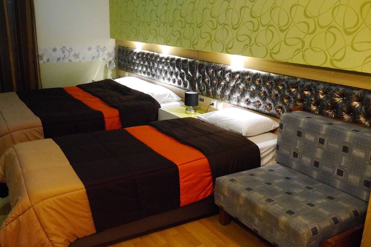 A hotel room with two beds, a nightstand, a lamp, and a patterned headboard.