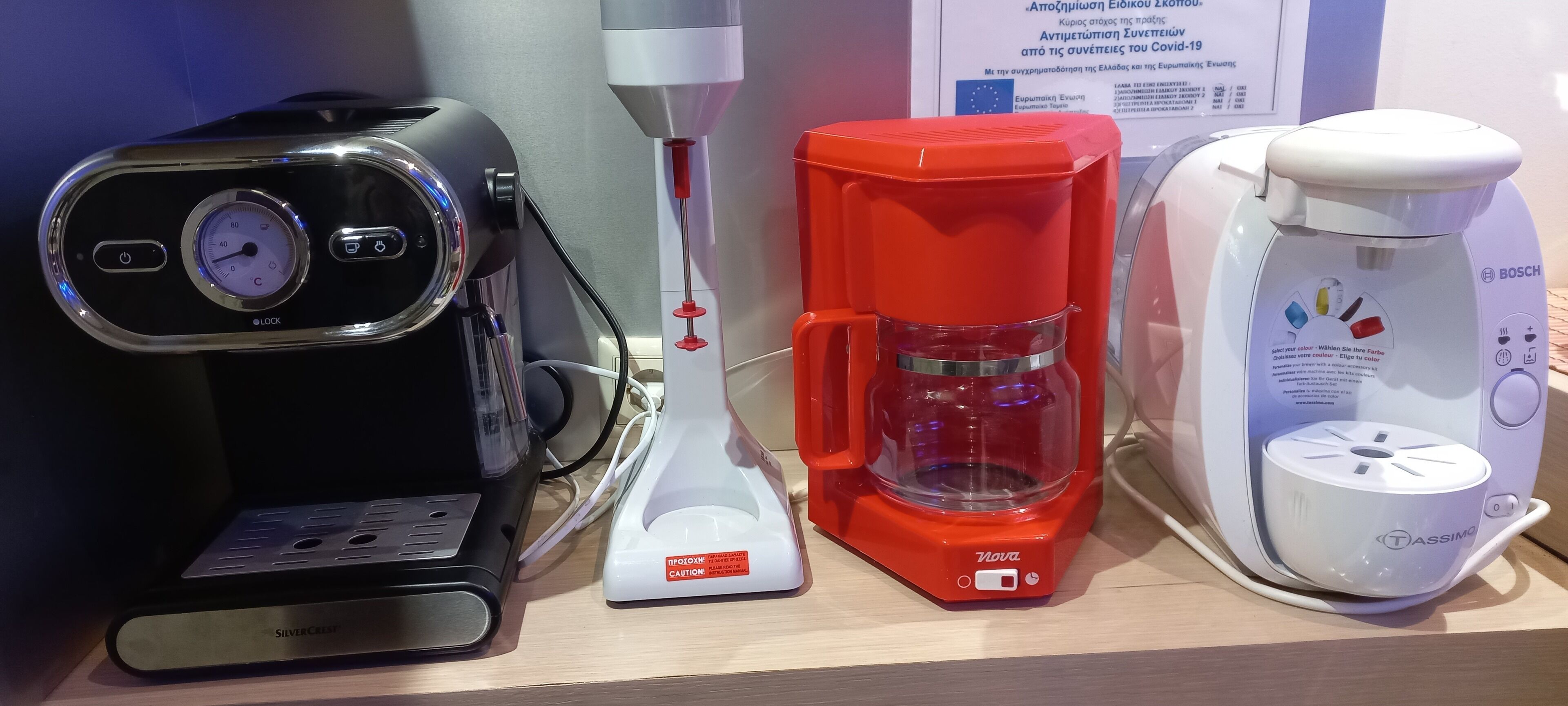 A coffee maker, a red coffee pot, and a white coffee maker on a shelf.