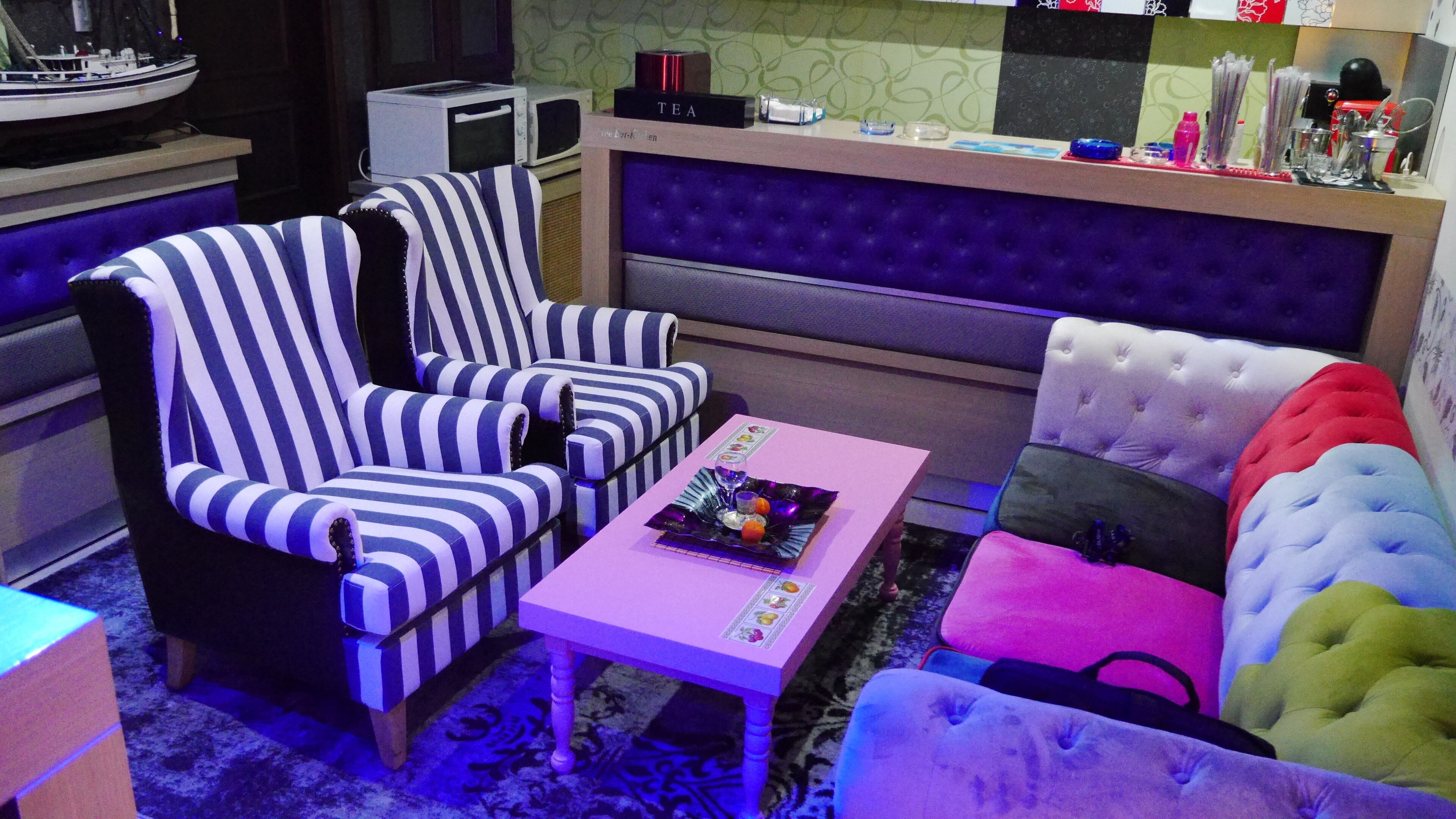 Une pièce avec des chaises à rayures, un canapé capitonné, une table rose et un four à micro-ondes posé sur un comptoir.