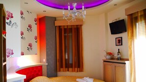 Una camera d'albergo con un letto, una televisione, un lampadario e una finestra con tende.