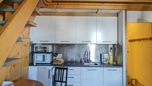 Una cocina compacta con armarios blancos, una escalera de madera y un comedor con mesa y sillas.