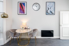 A modern dining area with a marble table, two chairs, a wall-mounted clock, and abstract art.