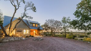 A two-story house with a stone foundation, a metal roof, and a gravel driveway. - Private Hilltop Farmhouse Incredible Views, Petting Zoo Animals & Hot Tub (Fredericksburg)