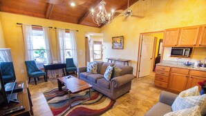 A living room with a sofa, armchairs, a coffee table, and a rug. There's a dining table with chairs, a kitchen area with a microwave, and a door leading outside. - Private Hilltop Farmhouse Incredible Views, Petting Zoo Animals & Hot Tub (Fredericksburg)