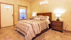 A bedroom with a bed, bedside tables, a nightstand, a window with curtains, an air conditioning unit, and a door. - Private Hilltop Farmhouse Incredible Views, Petting Zoo Animals & Hot Tub (Fredericksburg)