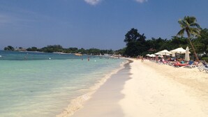 A beach with clear turquoise water, white sand, and palm trees. There are umbrellas and people on the beach. - The Point, Negril -1 BR, Ocean & beaches, Pool, Tennis, Snorkel 5 star location! (Negril)