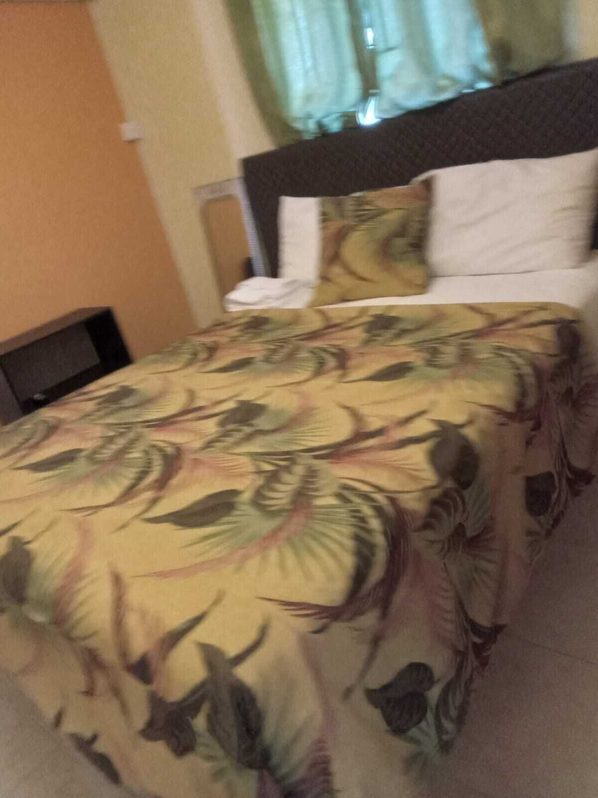 Quarto de hotel com cama, mesa de cabeceira e janela com cortinas.