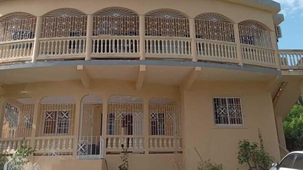 A two-story building with a balcony on the upper floor, featuring decorative railings and barred windows. - Unity Villa (Montego Bay)