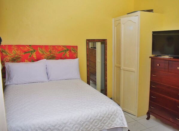 A bedroom with a bed, a wardrobe, a television, and a mirror.