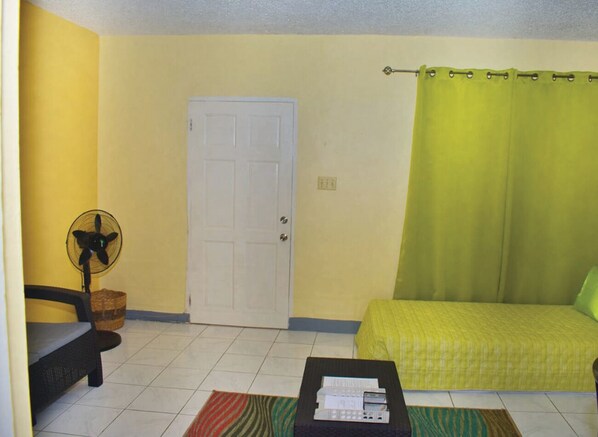 Una habitación con cama, ventilador, puerta y ventana con cortina.