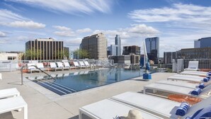 Zona de piscina en la azotea con sillones, piscina y edificios de la ciudad al fondo.