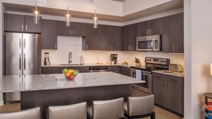 Una cocina moderna con armarios de madera oscura, electrodomésticos de acero inoxidable, una isla de granito con taburetes altos e iluminación colgante.