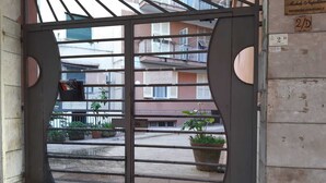 En metalport med netting, der fører til en balkon med plantekasser og udsigt til en boligbygning.