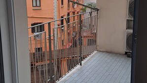 En balkon med gelænder i metal, flisegulv og udsigt til omkringliggende bygninger.