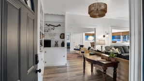 Amplia sala de estar con piso de madera, una mesa de comedor y un sofá. Un candelabro cuelga del techo y una ventana ofrece vistas al exterior.
