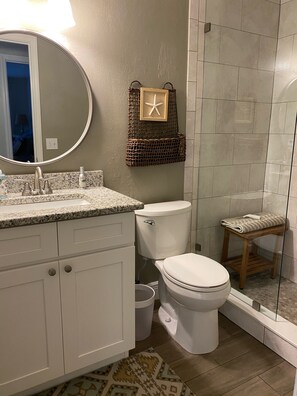 A bathroom with a white vanity, a round mirror, a wicker basket with a starfish, a toilet, and a glass-enclosed shower area. - IMPECCABLE CRYSTAL RIVER KING'S BAY WATERFRONT RETREAT - COMFORT & SERENITY (Crystal River)