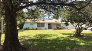 A single-story house with a front lawn, a large tree in the foreground, and a clear sky. - IMPECCABLE CRYSTAL RIVER KING'S BAY WATERFRONT RETREAT - COMFORT & SERENITY (Crystal River)