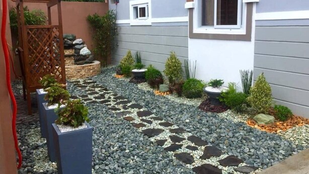 A garden with a stone pathway, various potted plants, and a wooden pergola.