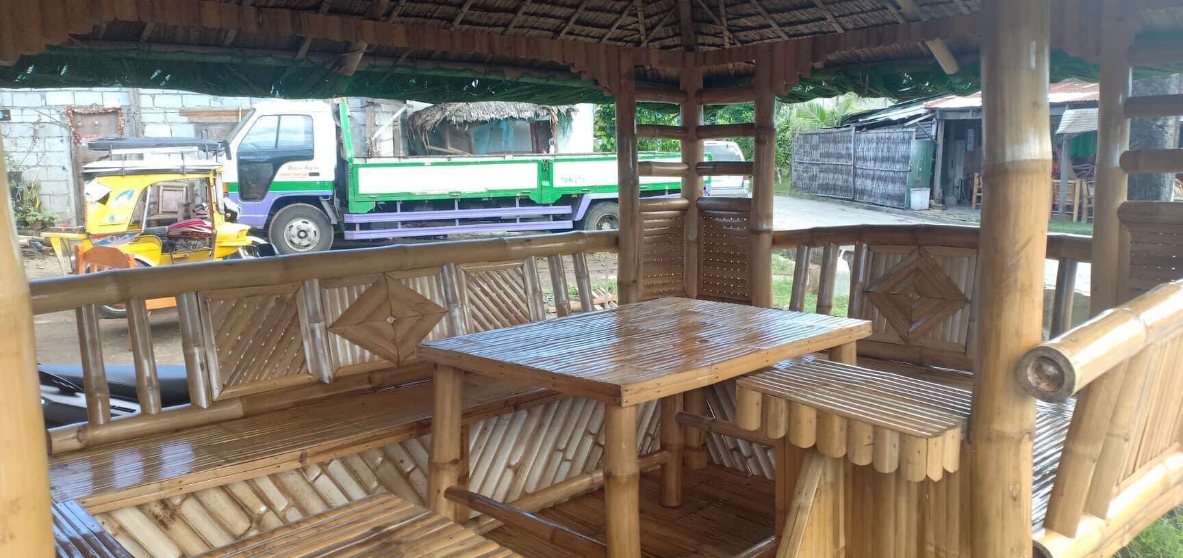 A wooden structure with a table and benches, a thatched roof, and a view of a street with vehicles.