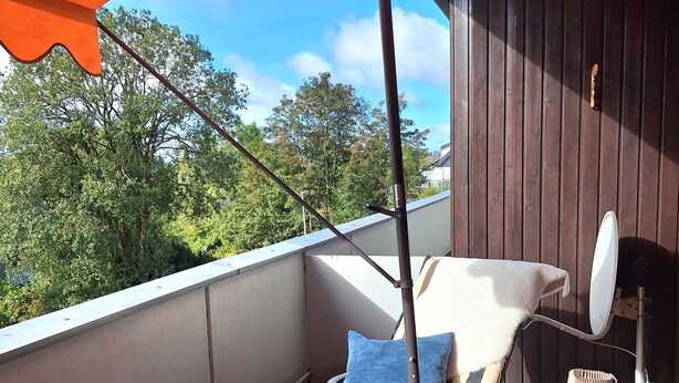 Un balcón con una silla colgante, una mesita con lámpara y vistas a árboles.