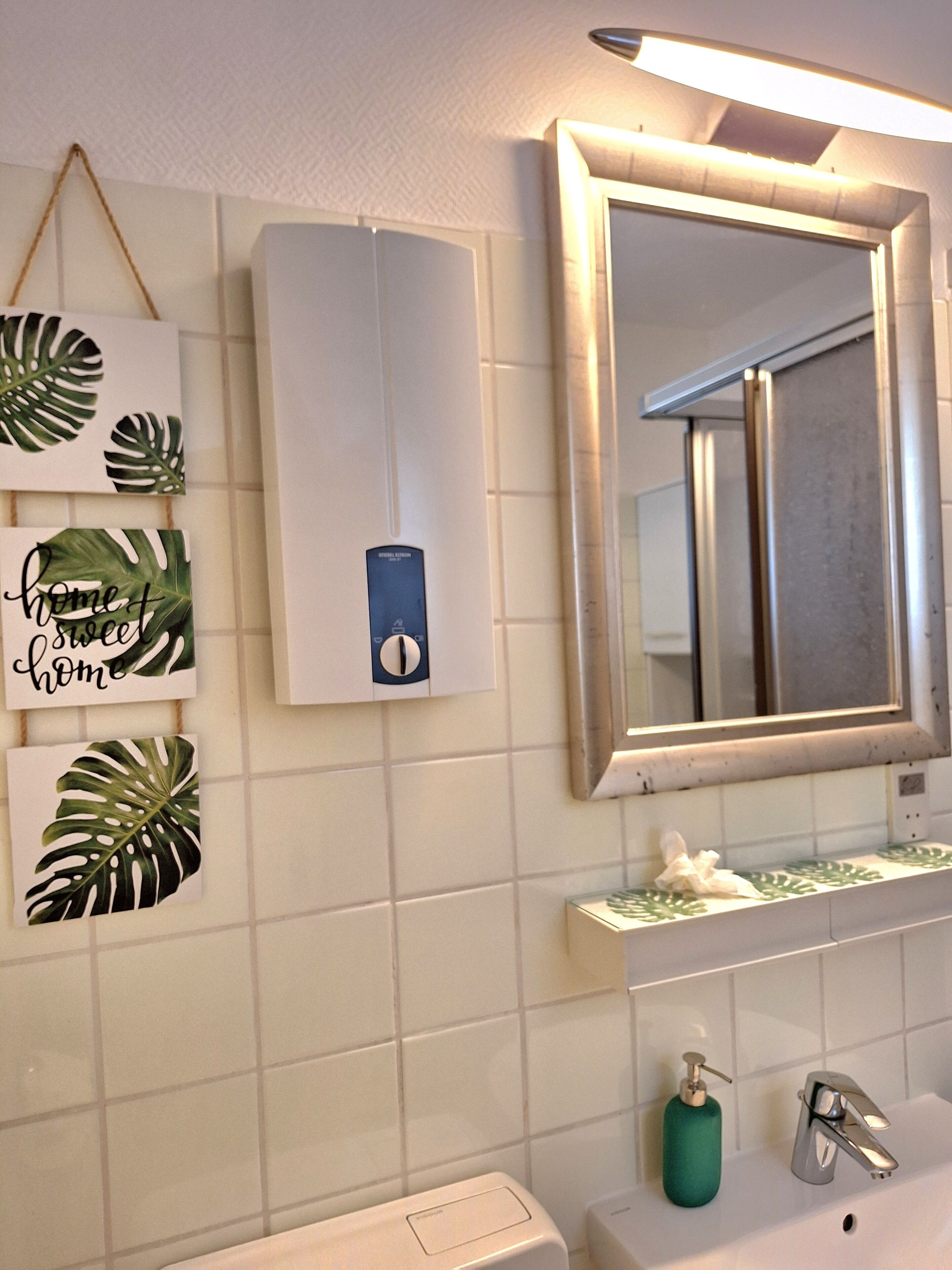 Ein Badezimmer mit einem weißen Waschbecken, einem Spiegel, einem Händetrockner und einer Seifenspender.