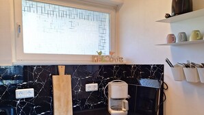 Una cocina con salpicadero de mármol, un tostador, una ventana con un cartel de bienvenida y una estantería con tazas.