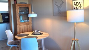 Un comedor moderno con una mesa redonda, dos sillas, un aparador de madera, una lámpara de pie y una luz empotrada en la pared.