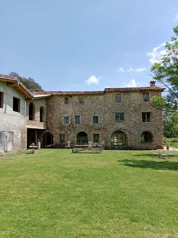 A stone building with a tiled roof, multiple windows, and a grassy courtyard with outdoor seating.