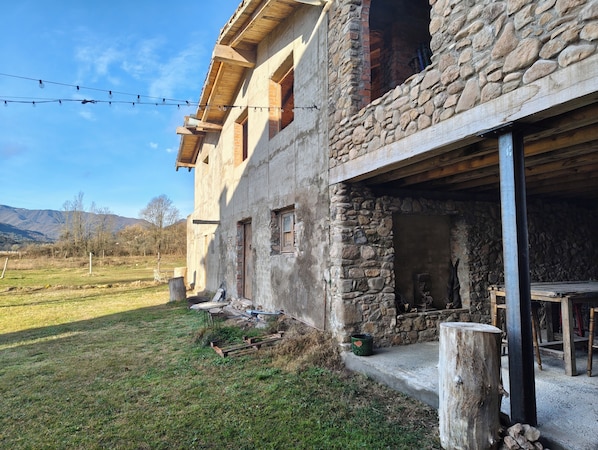 A rustic stone building with a wooden balcony, a stone fireplace, and a grassy yard.