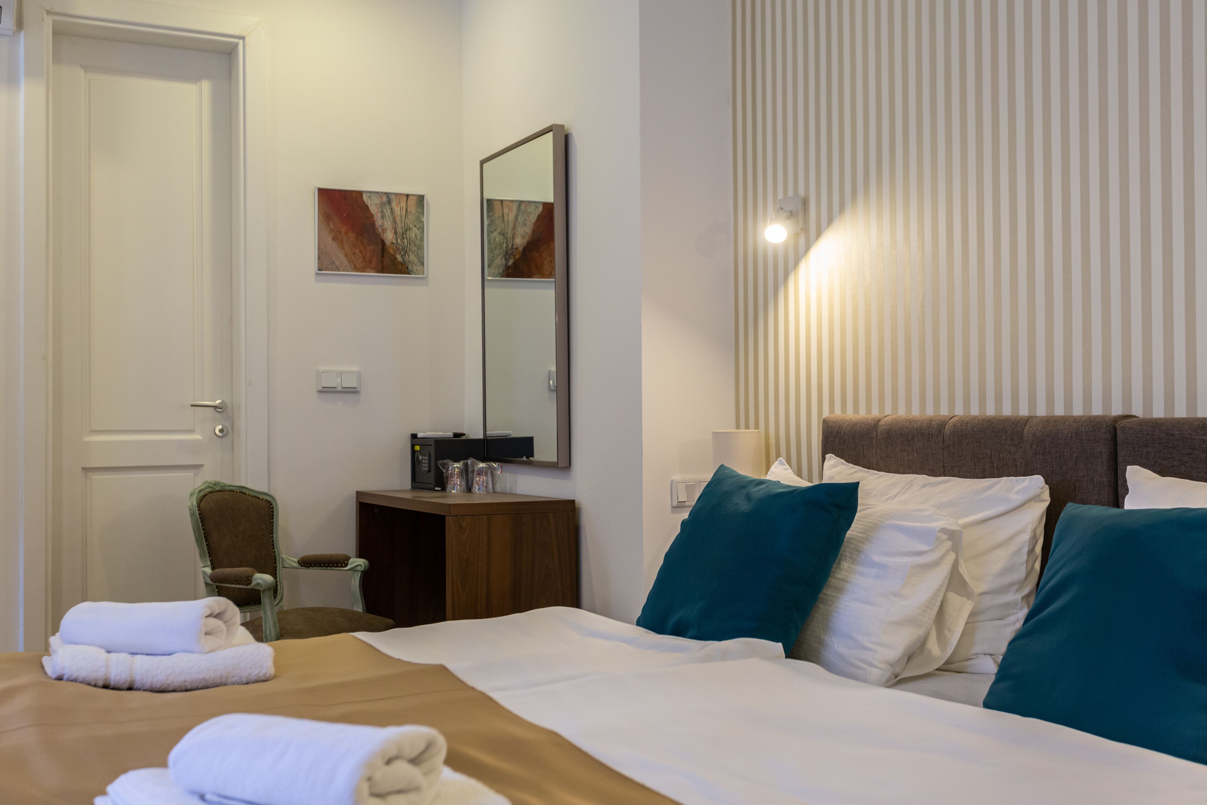 A hotel room with a bed, a chair, a desk, a mirror, and a window with blinds.