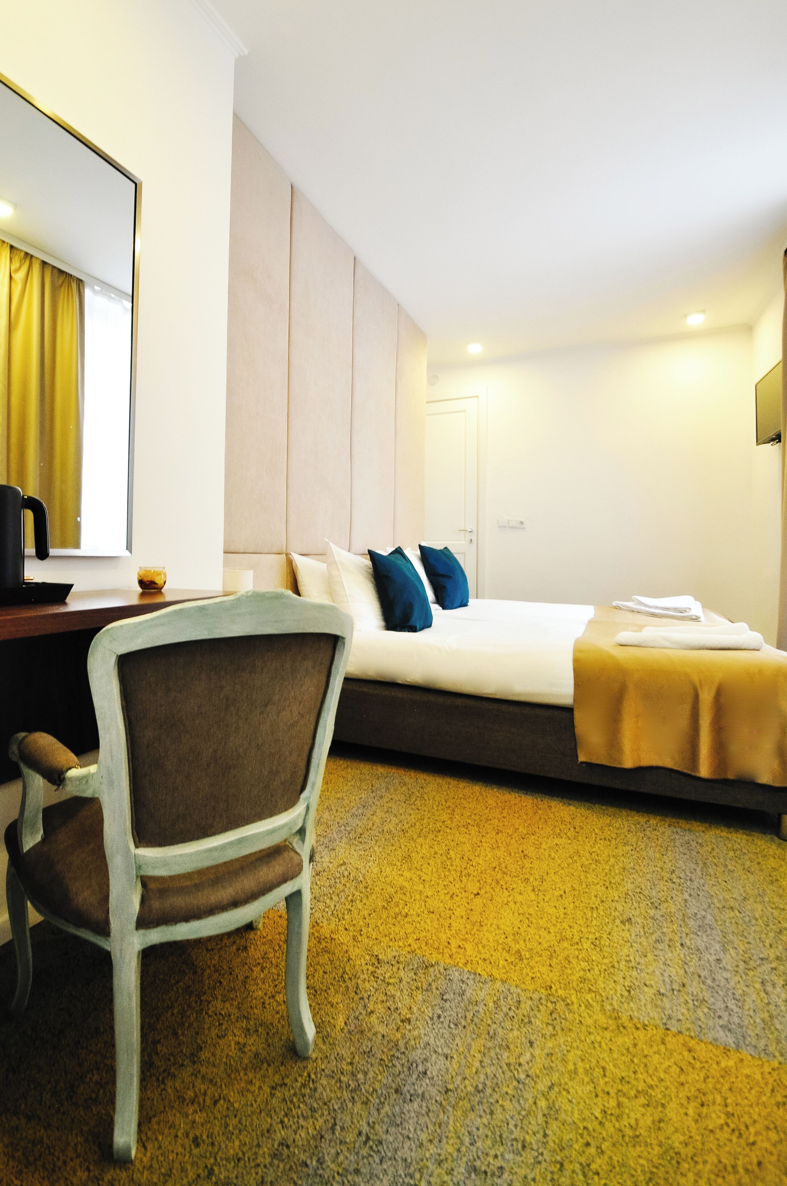 A hotel room with a bed, a desk with a chair, a mirror, and a window with curtains.