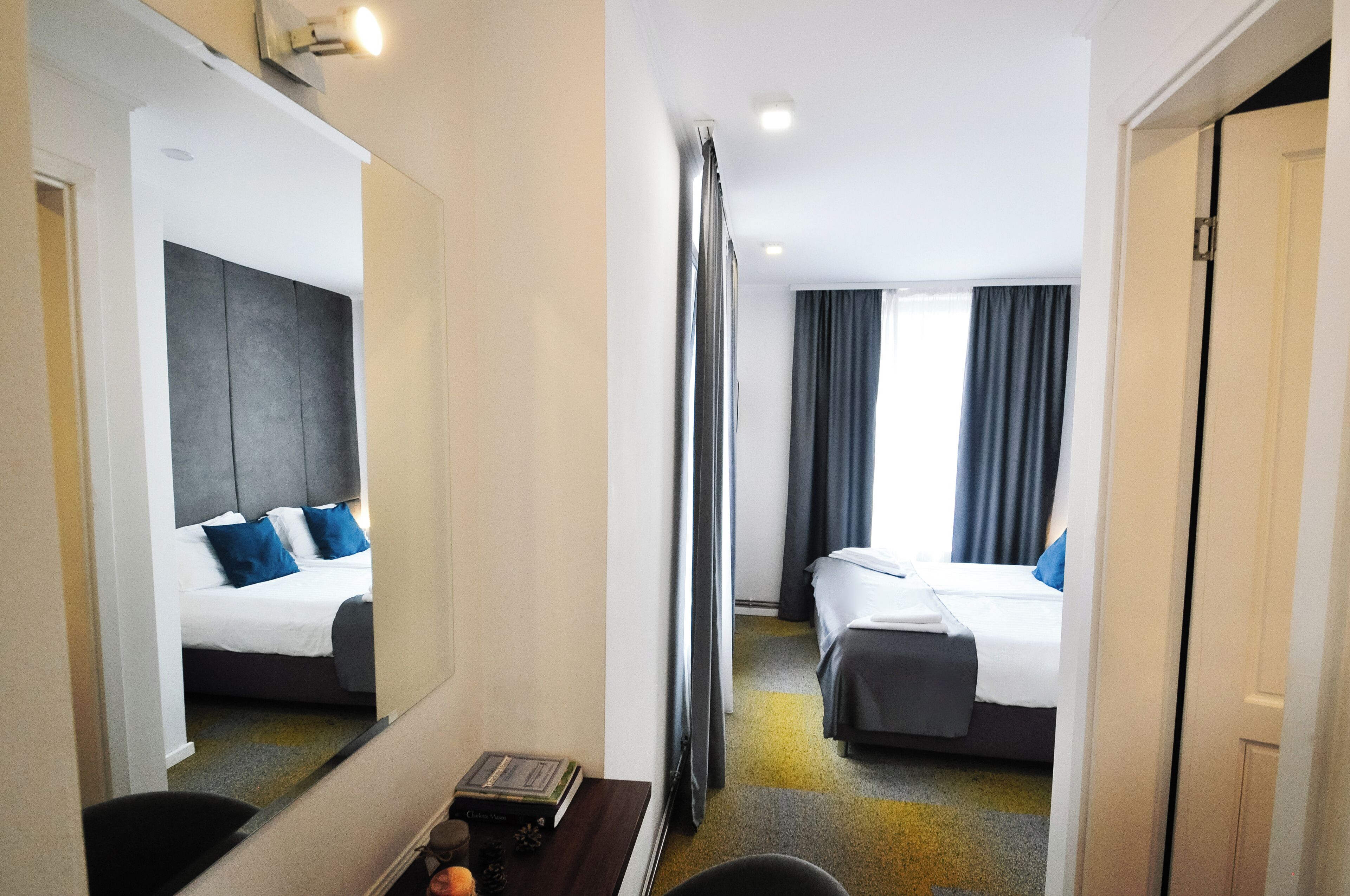 A hotel room with two beds, a large mirror, a small table with a book, and a view of the hallway.