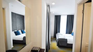 Quarto de hotel com duas camas, um espelho grande, uma mesa pequena com um livro e vista para o corredor.